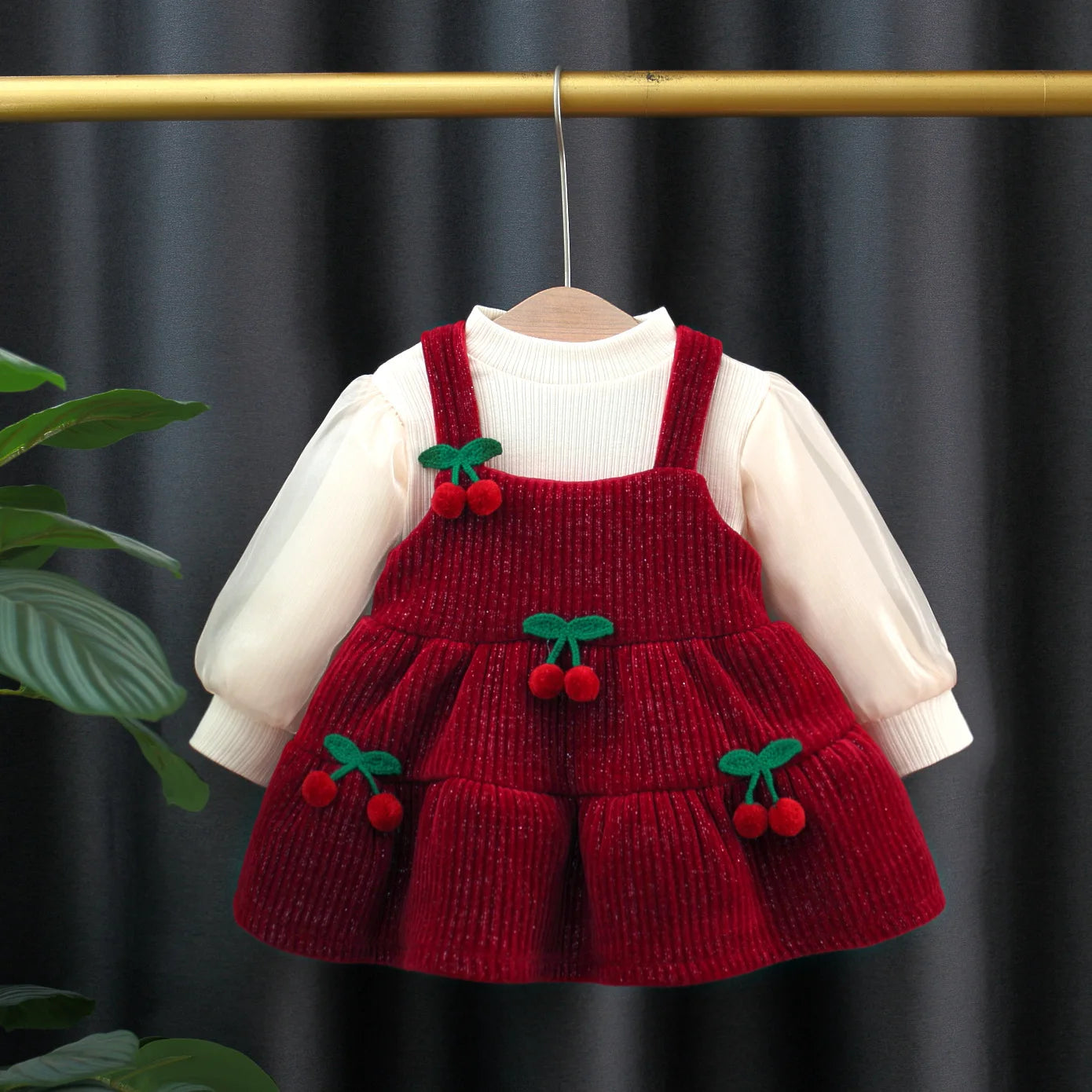 Red knitted dress with cherry details on a hanger against a dark background