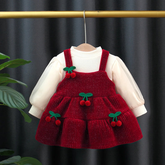 Red knitted dress with cherry details on a hanger against a dark background