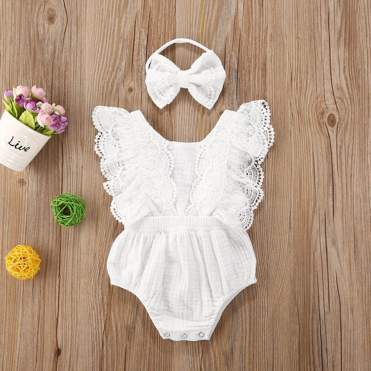 White lace baby romper with matching headband on a wooden surface with decorative elements.
