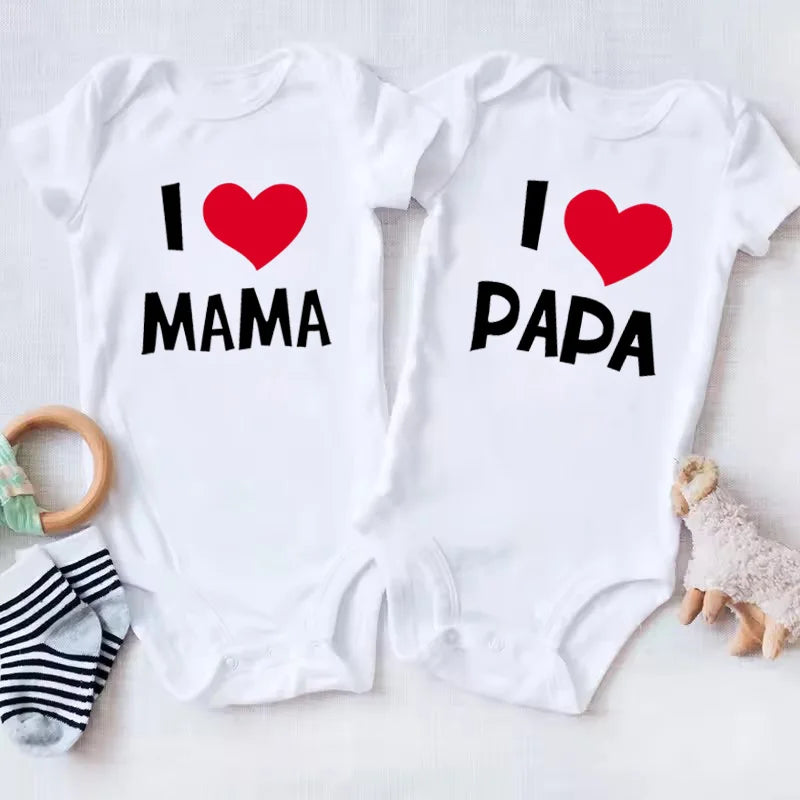 Two white baby onesies with 'I ❤️ MAMA' and 'I ❤️ PAPA' text on a light gray background.