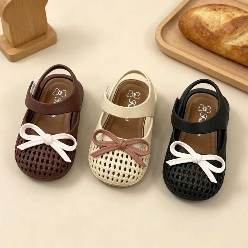 Three pairs of children's sandals in brown, beige, and black with bow details on a light background.