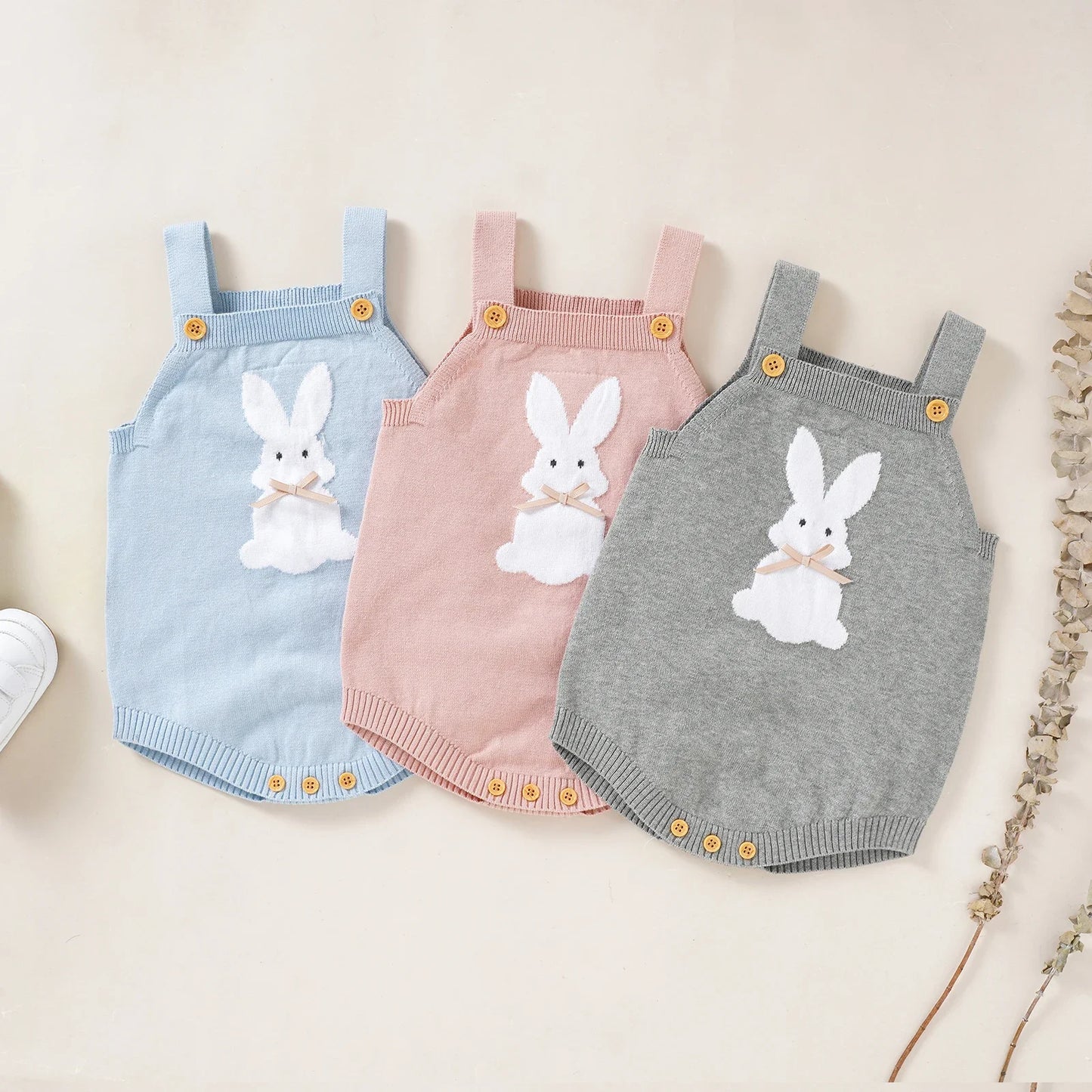 Three baby rompers with bunny designs in blue, pink, and gray on a light background.