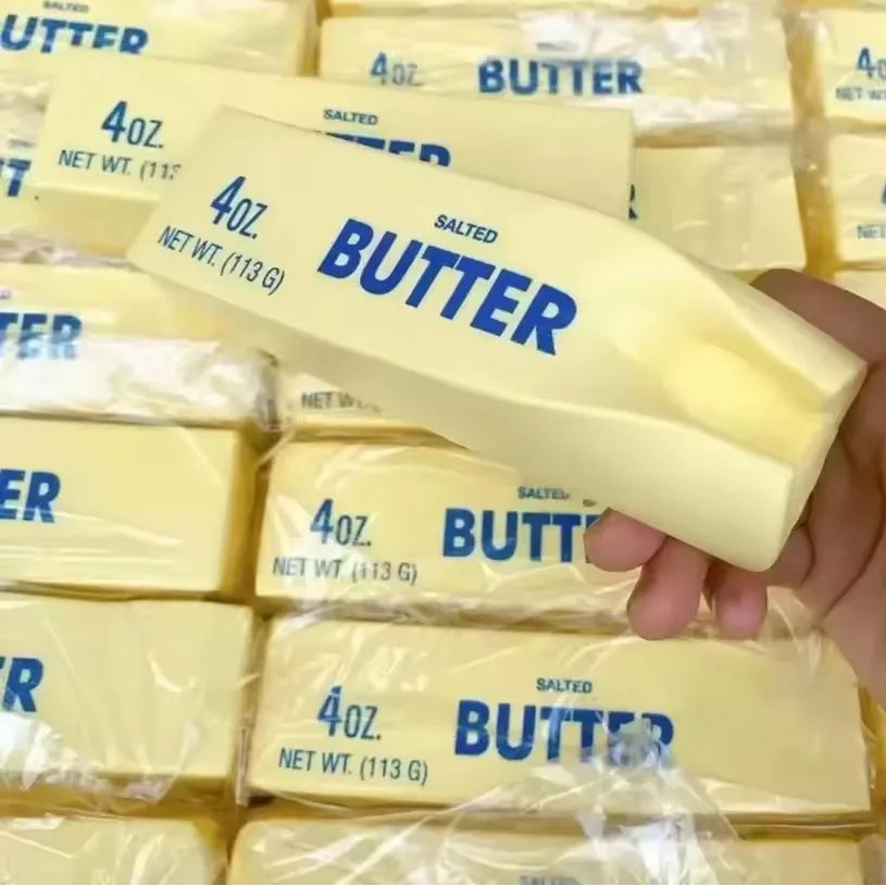 Hand holding a 4 oz block of butter with stacked butter packages in the background.
