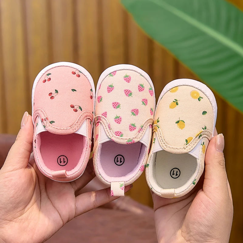 Three pairs of baby shoes with fruit patterns held by a hand against a blurred background.