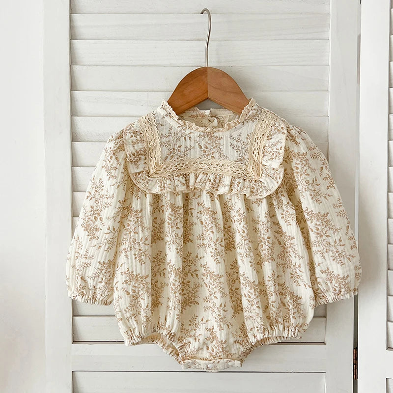 Floral lace baby romper on a wooden hanger against a white paneled wall.