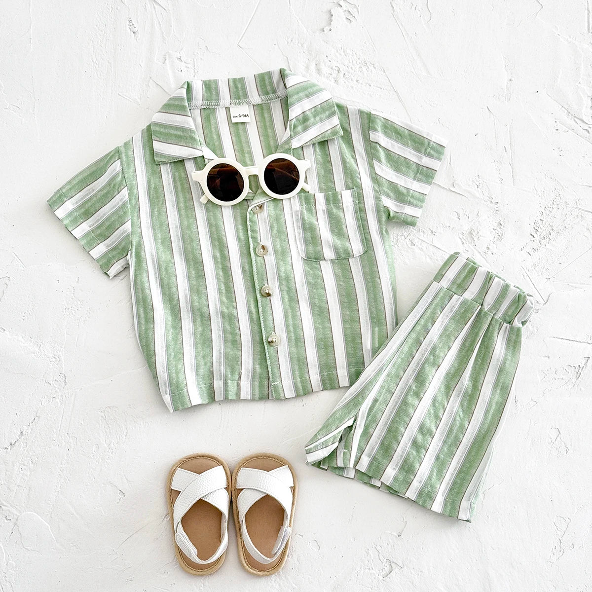 Green and white striped shirt and shorts set with sunglasses and sandals on a light gray background