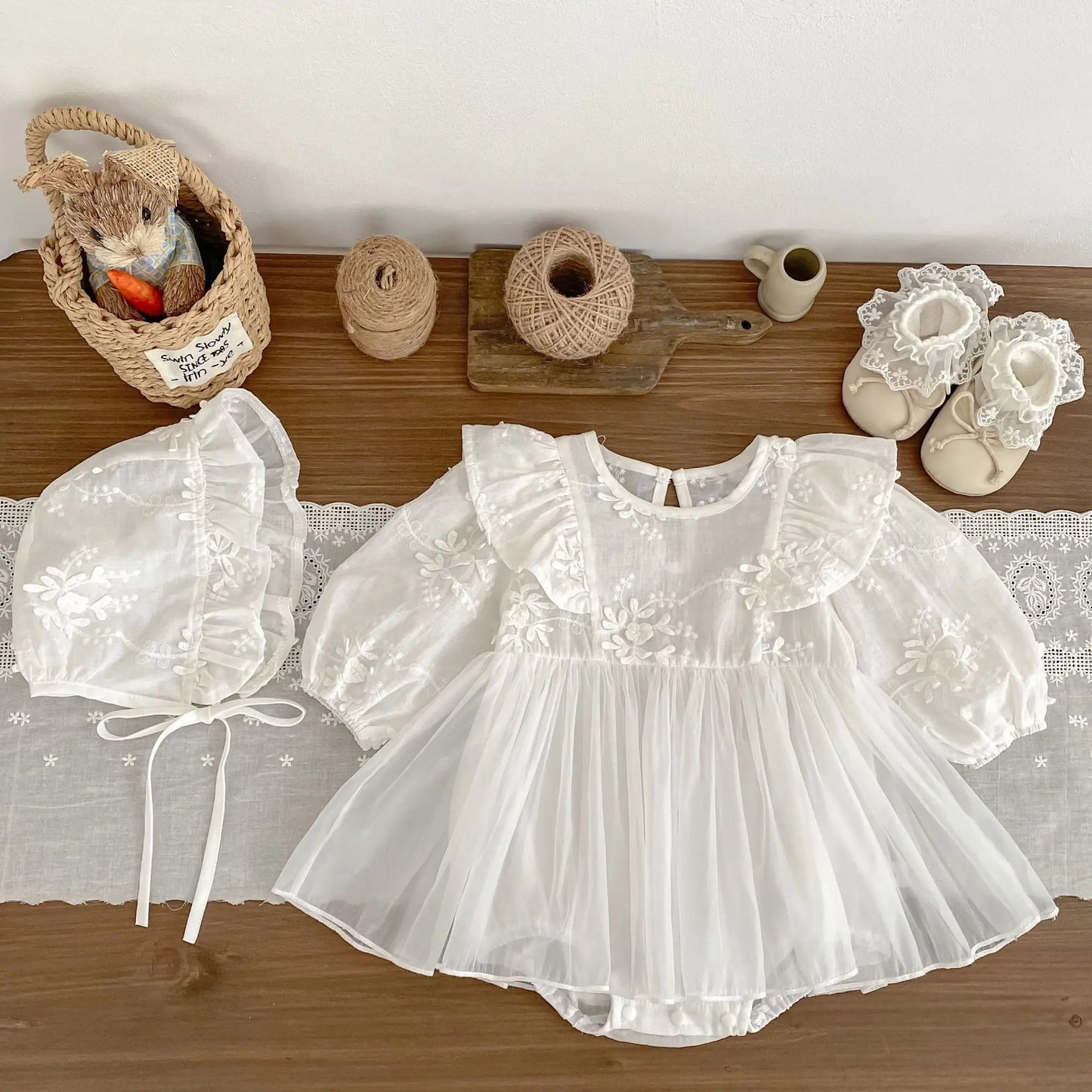White baby dress with bonnet and shoes on a wooden surface