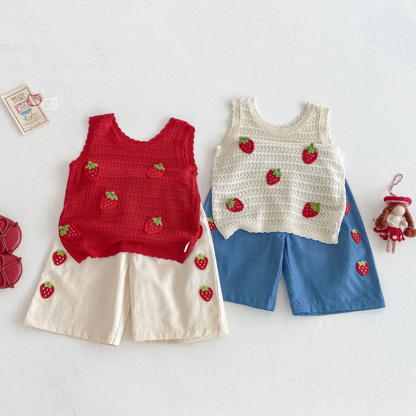 Two children's outfits with strawberry patterns on a white background