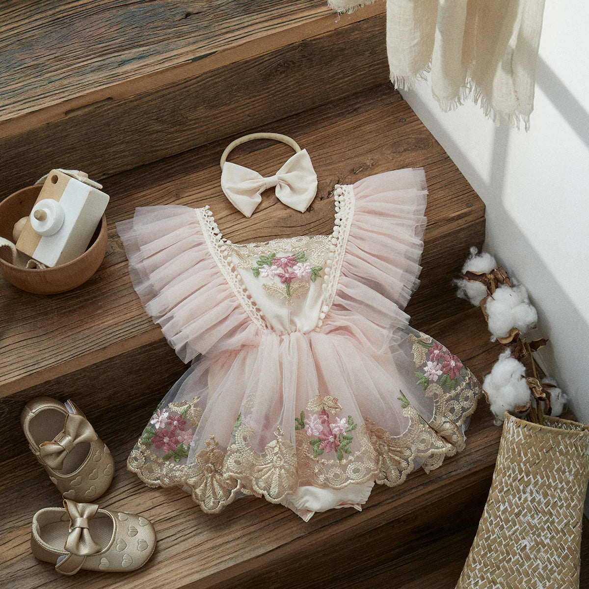 Children's pink dress with floral patterns on a wooden surface, accompanied by shoes and a headband.
