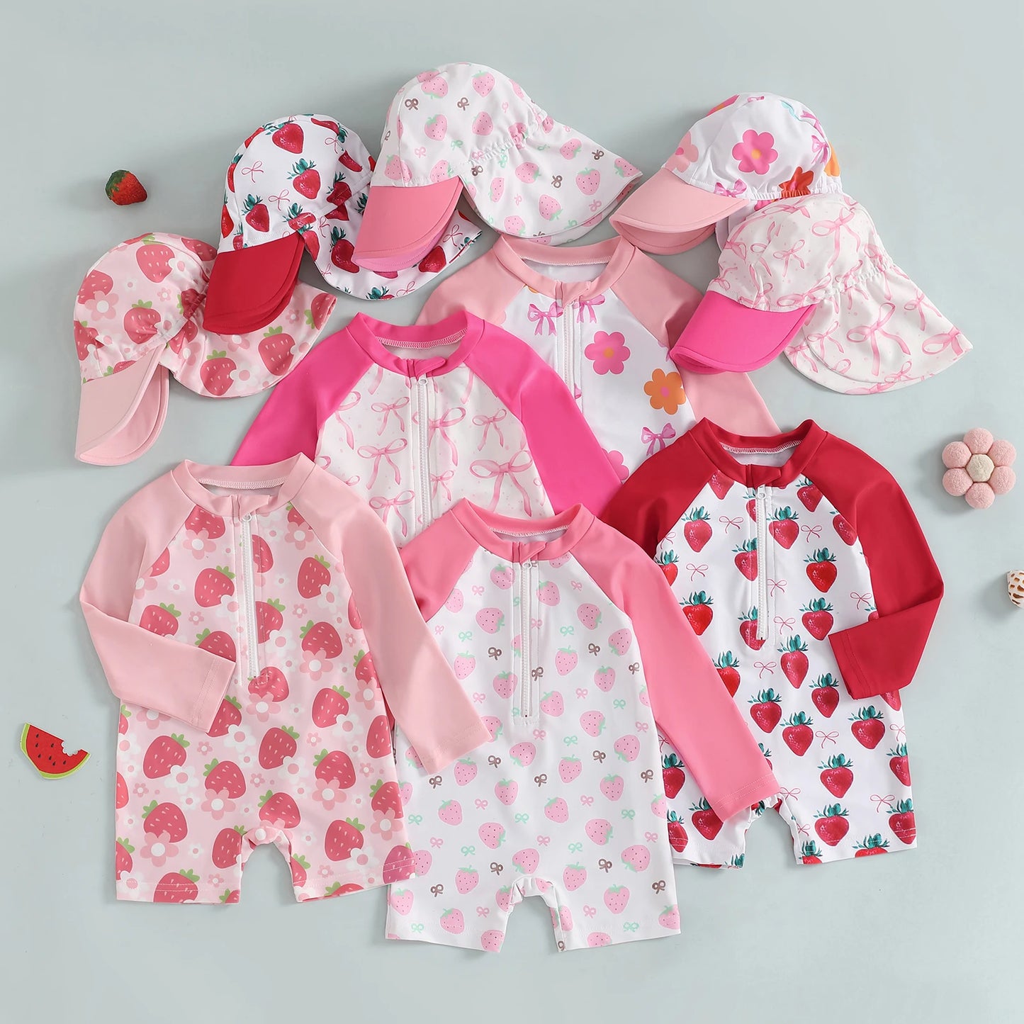 Collection of children's strawberry-patterned swimwear and hats on a gray background