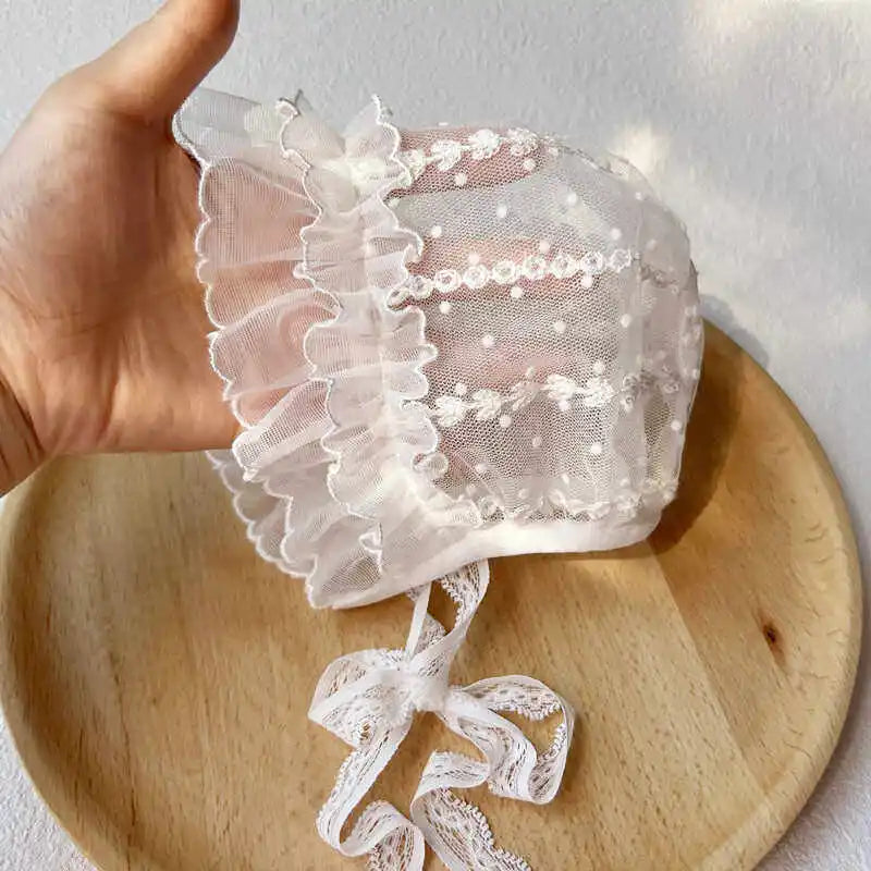 White lace bonnet held by a hand on a wooden surface with a light gray background