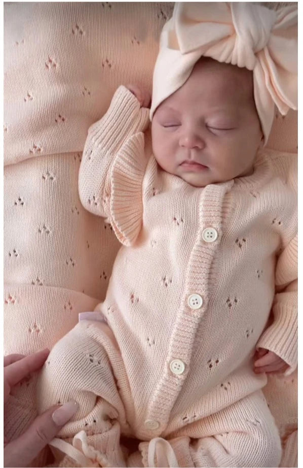 Newborn baby in a pink outfit with a matching headband on a soft pink background