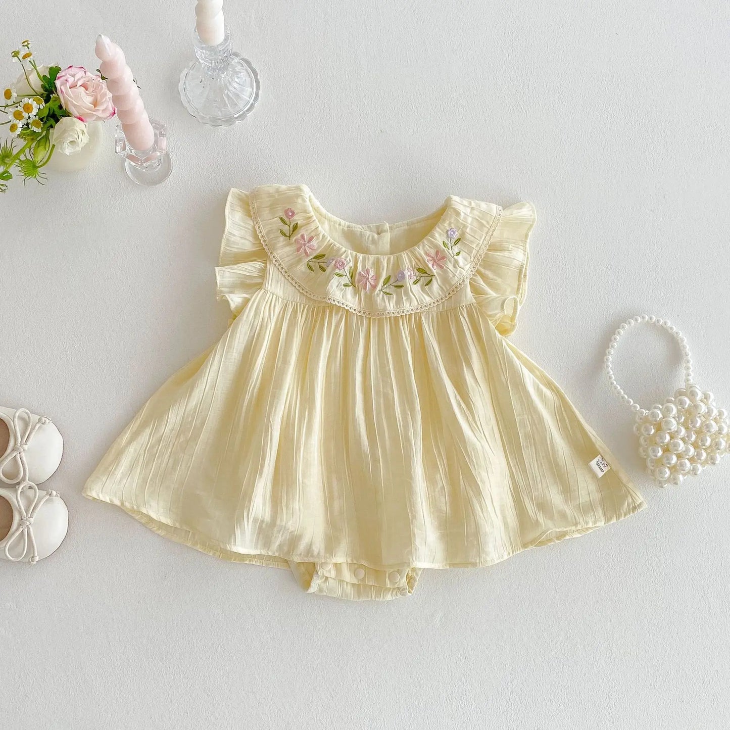 Yellow baby dress with floral embroidery on a light gray background
