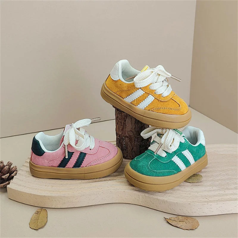 Three children's sneakers in pink, yellow, and green on a wooden surface with a neutral background.