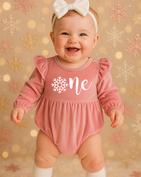 Baby girl in a pink
 ‘Onederland’ snowflake outfit, standing beside a fluffy stool on a soft lavender background — perfect for a snowflake Onederland 1st birthday cake smash photoshoot.
